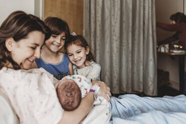 Side view of mother holding newborn son meeting siblings - CAVF77679