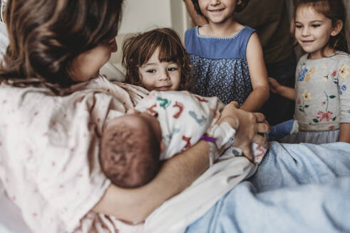 Seitenansicht einer Mutter, die ihren neugeborenen Sohn hält und auf Geschwister trifft - CAVF77681