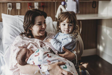 Mid view of mother holding newborn son meeting siblings - CAVF77686