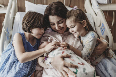 Mid view of mom and daughters holding newborn son - CAVF77695