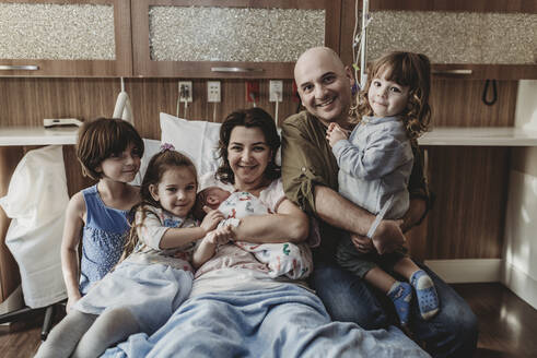 Mittelansicht der ganzen Familie, die ihren neugeborenen Sohn hält und im Krankenhaus lächelt - CAVF77697