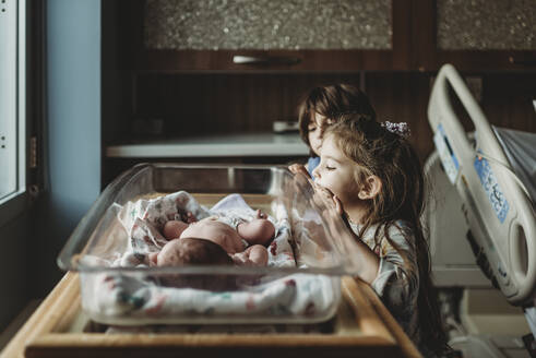 Schwestern betrachten ihren neugeborenen Bruder im Stubenwagen des Krankenhauses - CAVF77719