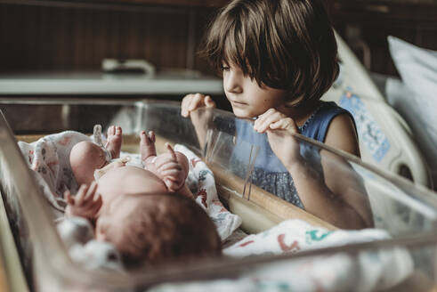 Schwester betrachtet neugeborenen Bruder im Stubenwagen des Krankenhauses - CAVF77721