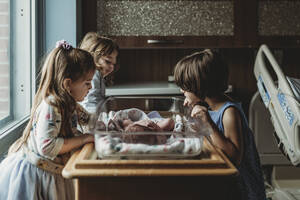 Geschwister betrachten ihren neugeborenen Bruder im Stubenwagen des Krankenhauses - CAVF77722