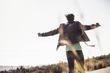 Rear view of man with outstretched arms on country road - SDAHF00670