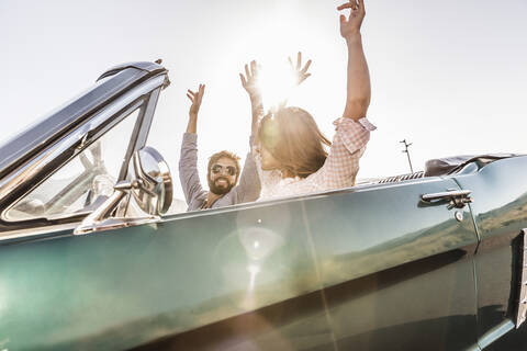 Glückliches Paar mit erhobenen Armen im Cabrio auf einer Autoreise, lizenzfreies Stockfoto