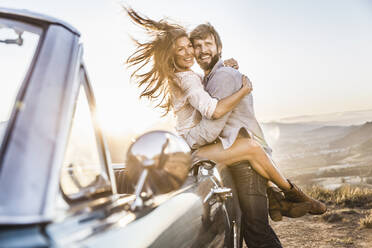 Happy couple at convertible car in the countryside at sunset - SDAHF00718