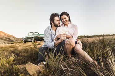 Affectionate couple sitting on meadow in the countryside having a glass of white wine - SDAHF00722