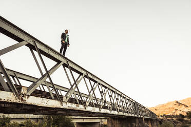 Mann steht auf dem Metallbalken einer alten Eisenbahnbrücke - SDAHF00747