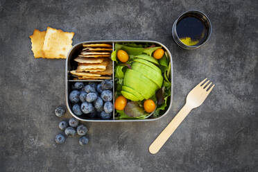 Schüssel mit Salatdressing und Lunchbox mit Avocadoscheiben, gelben Tomaten, Crackern, Blaubeeren und grünem Salat - LVF08696