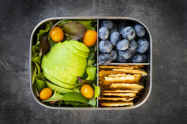 Lunch box with sliced avocado, yellow tomatoes, crackers, blueberries and green salad - LVF08697