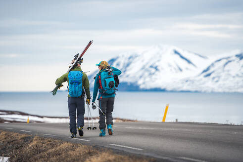 Ein Paar geht mit einer Skiausrüstung eine Straße in Island entlang - CAVF77775