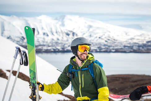 A man with backpack, radio, and skis with mountains behind him - CAVF77786