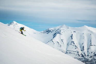 Ein Mann beim Skifahren mit Bergen im Rücken in Island - CAVF77788