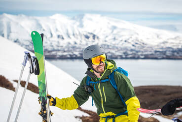 Ein Mann mit Skiausrüstung und Bergen und Wasser im Rücken - CAVF77790