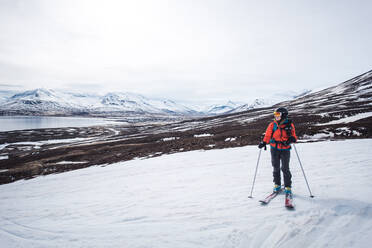 Eine Frau steht mit Skiern auf Schnee mit Bergen und Wasser im Hintergrund - CAVF77792