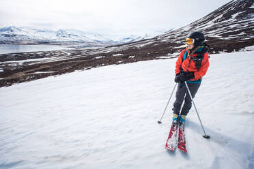 Eine Frau steht mit Skiern auf Schnee mit Bergen und Wasser im Hintergrund - CAVF77793