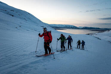 Eine Gruppe von Skifahrern bei Sonnenaufgang in Island mit Wasser im Hintergrund - CAVF77808