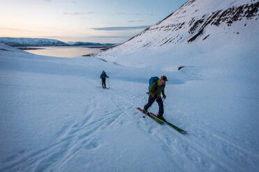 Man and woman backcountry skiing in Iceland with water behind - CAVF77810