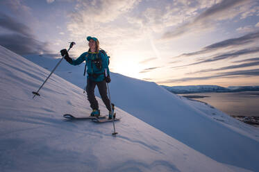 Frau beim Skilanglauf in Island bei Sonnenaufgang mit Wasser im Hintergrund - CAVF77826