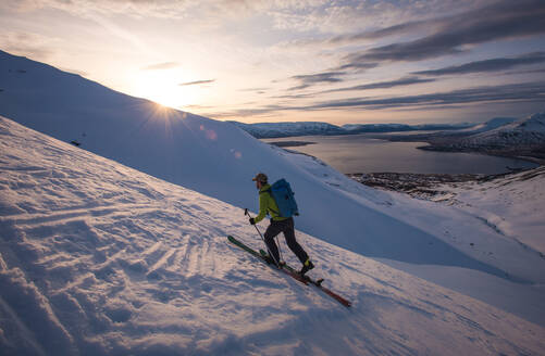 Mann beim Skifahren in Island bei Sonnenaufgang mit Wasser im Rücken - CAVF77828