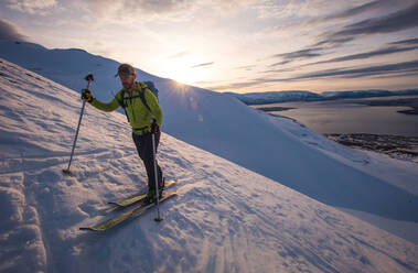 Mann beim Skifahren in Island bei Sonnenaufgang mit Wasser im Rücken - CAVF77830