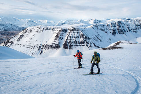 Mann und Frau beim Skifahren in Island mit Bergen im Hintergrund - CAVF77837