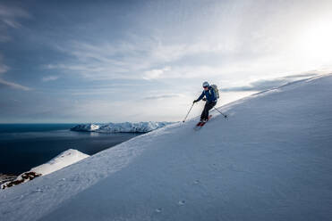 Ein Mann beim Skifahren bergab mit dem Meer im Hintergrund in Island - CAVF77839