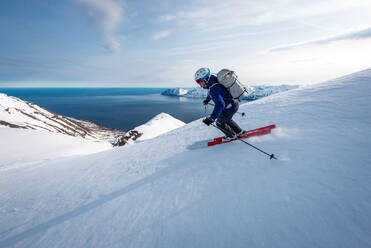 Ein Mann beim Skifahren bergab mit dem Meer im Hintergrund in Island - CAVF77840