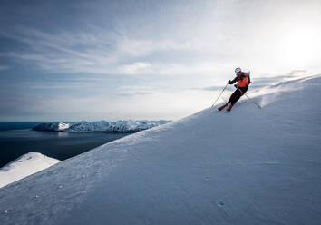 Ein Mann beim Skifahren bergab mit dem Meer im Hintergrund in Island - CAVF77842