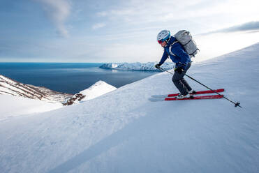 A man skiing downhill with ocean in the background in Iceland - CAVF77843