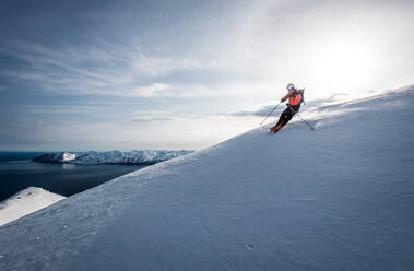 Ein Mann beim Skifahren bergab mit dem Meer im Hintergrund in Island - CAVF77844