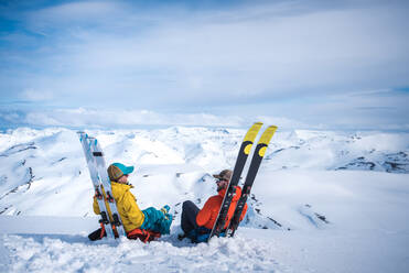 Frau und Mann sitzen auf Skiern mit Bergen im Hintergrund - CAVF77871