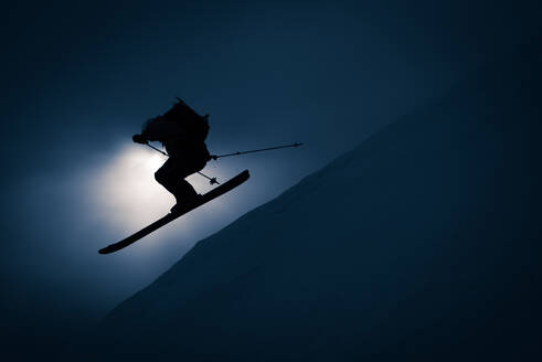 Silhouette eines Mannes, der mit Skiern und Rucksack von der Schanze geht - CAVF77873