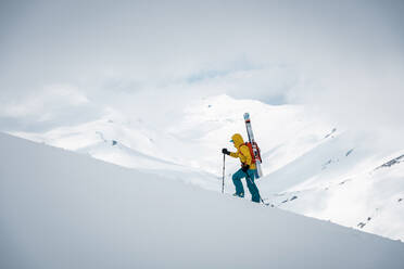 A person walks up a mountain ridge with skis on her back - CAVF77886