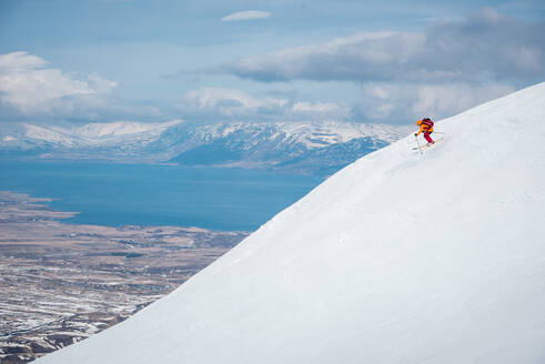 Ein Mann springt von einer Skisprungschanze auf einem Berg in Island mit Wasser im Rücken - CAVF77889