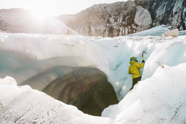 Side view of man ice climbing outside of glacial cave. - CAVF77935