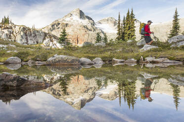 Side view and reflection of backpacker hiking beside alpine lake. - CAVF77940