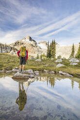 Rear view and reflection of backpacker looking at mountain summit. - CAVF77942