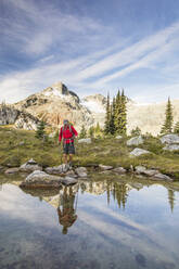 Reflection of backpacker balancing on rocks next to alpine lake. - CAVF77943