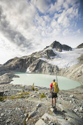 Backpacker stops to look at view of mountains glacier and lake. - CAVF77952