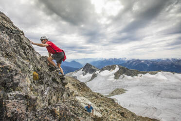 Two climbers scramble up a rocky cliff in the mountains.. - CAVF77958