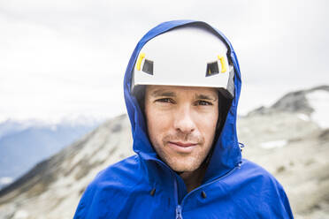 Porträt eines Bergsteigers mit Helm und Regenjacke. - CAVF77973