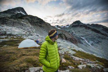 Wanderer steht neben dem Zelt und blickt auf die Berge. - CAVF77983