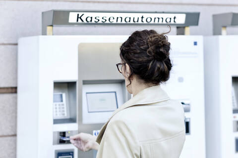 Rückansicht einer reifen Frau, die einen Geldautomaten benutzt, lizenzfreies Stockfoto