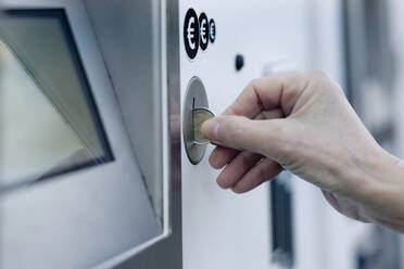 Frauenhand, die eine Münze in einen Münzautomaten wirft - FLLF00439