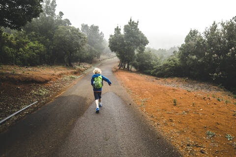 Rückenansicht eines kleinen Jungen mit Rucksack auf der Landstraße, La Gomera, Kanarische Inseln, Spanien, lizenzfreies Stockfoto