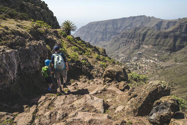 Back view of father and little son with backpacks walking on a hiking trail in the mountains, La Gomera, Canary Islands, Spain - IHF00293