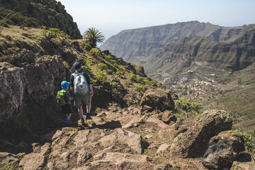 Rückenansicht von Vater und kleinem Sohn mit Rucksäcken auf einem Wanderweg in den Bergen, La Gomera, Kanarische Inseln, Spanien - IHF00293