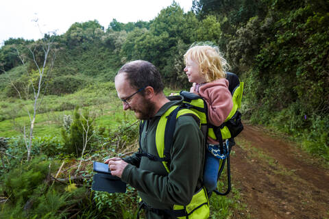 Father carrying his little daughter in a child carrier on a hiking trail, using smartphone, Canary Islands, La Palma, Spain stock photo